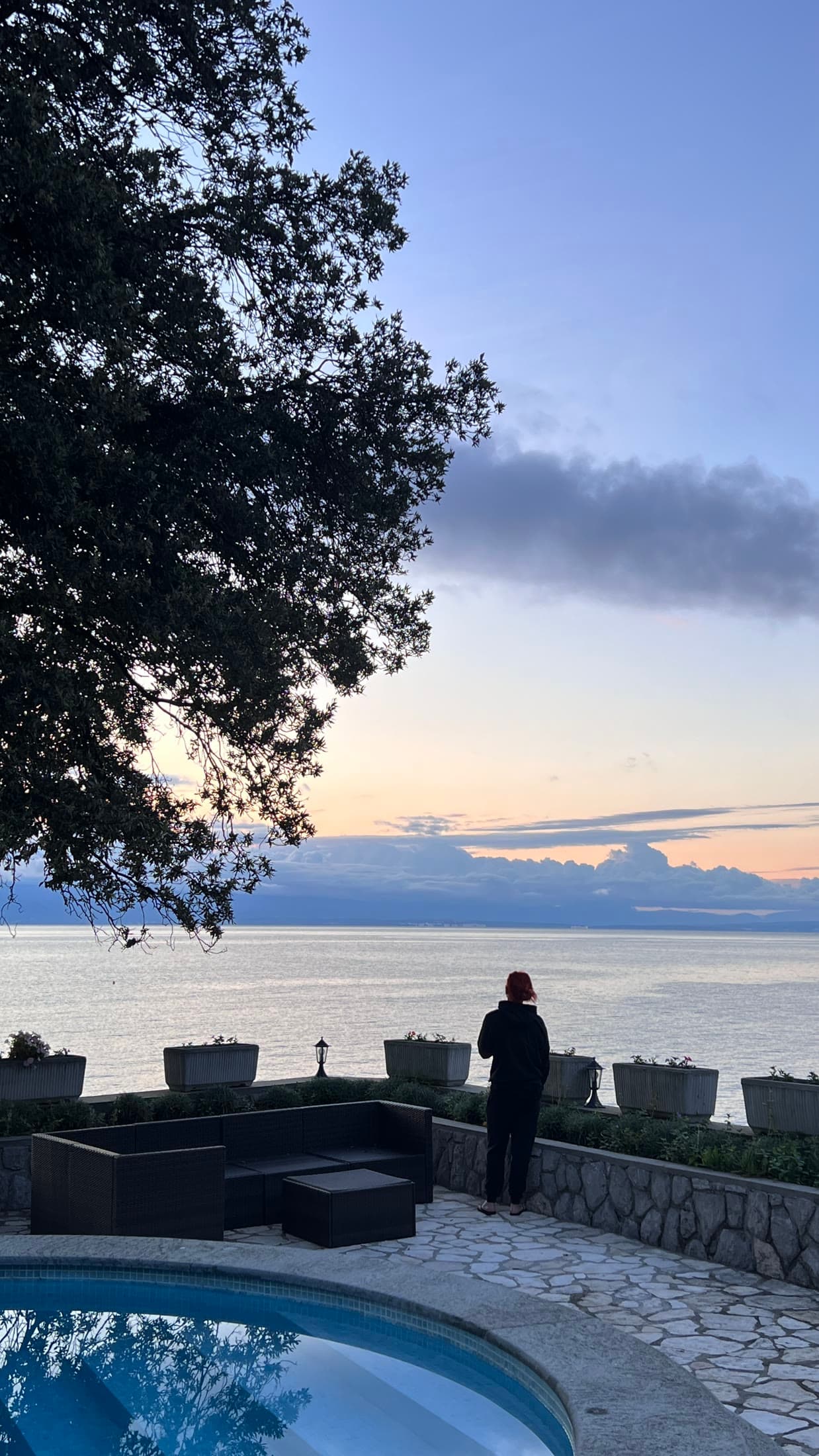 A solitary figure standing at dusk on a terrace, looking out over still water
