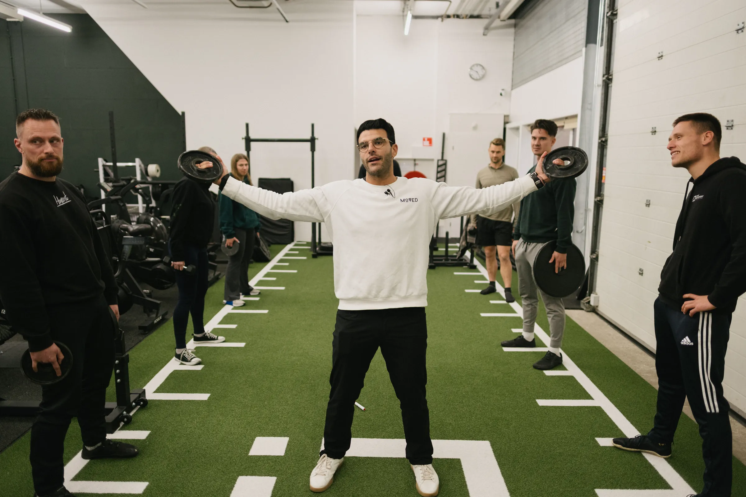 Richard Aceves demonstrating a plate hold on gym turf while a circle of coaches watches