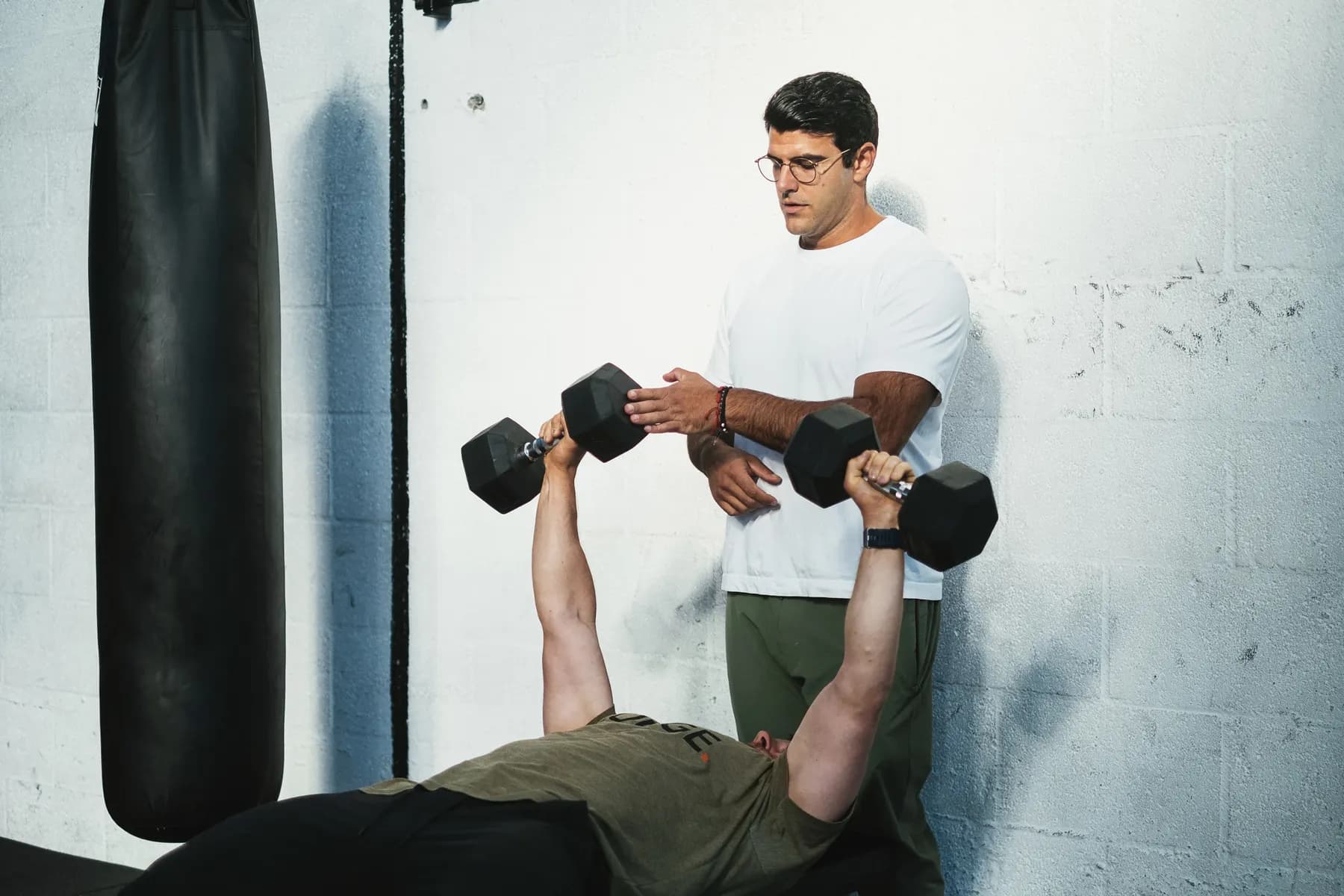 Richard Aceves watching a client hold a sandbag, checking how the body carries the load