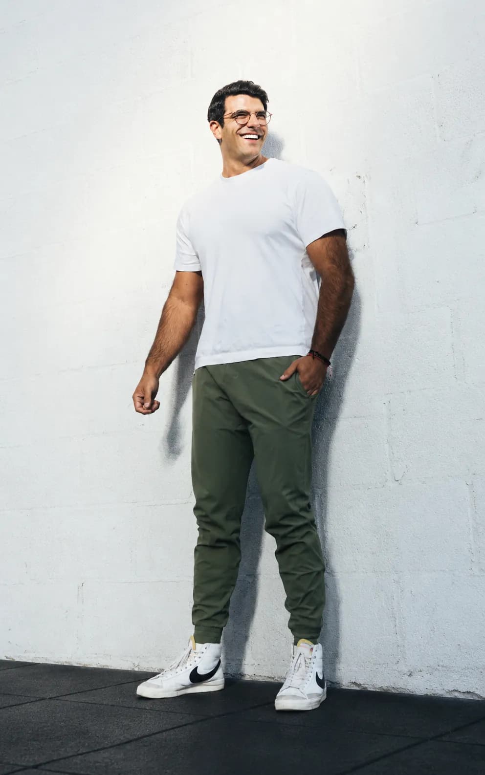 Richard Aceves standing relaxed against a white wall, mid-laugh